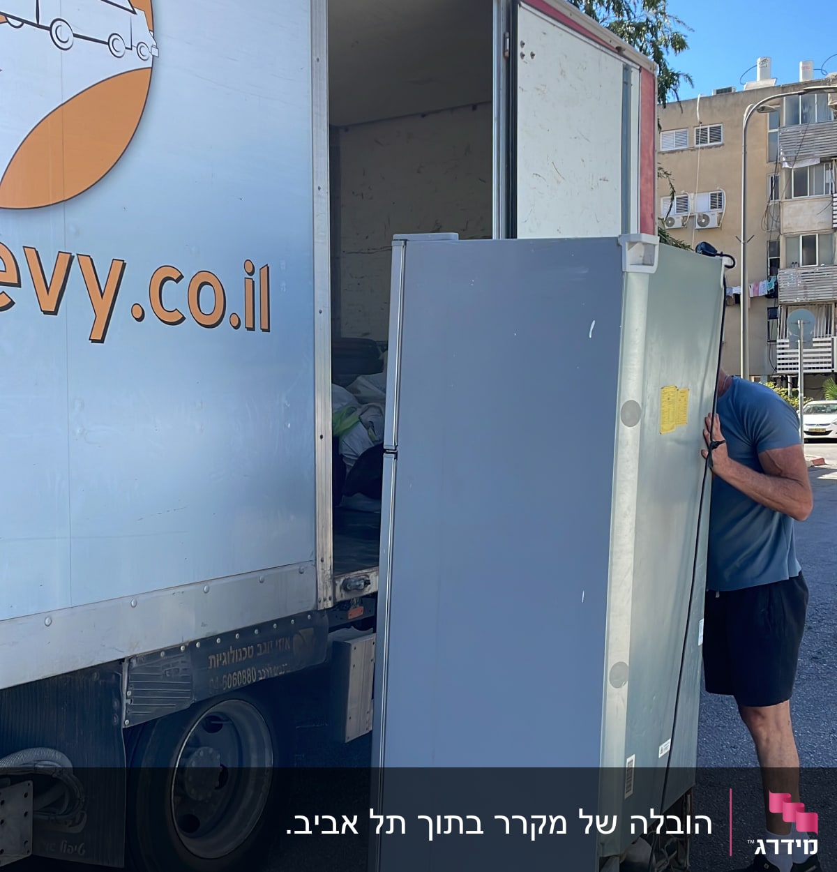 אדם מעמיס מקרר למשאית הובלה ברחוב